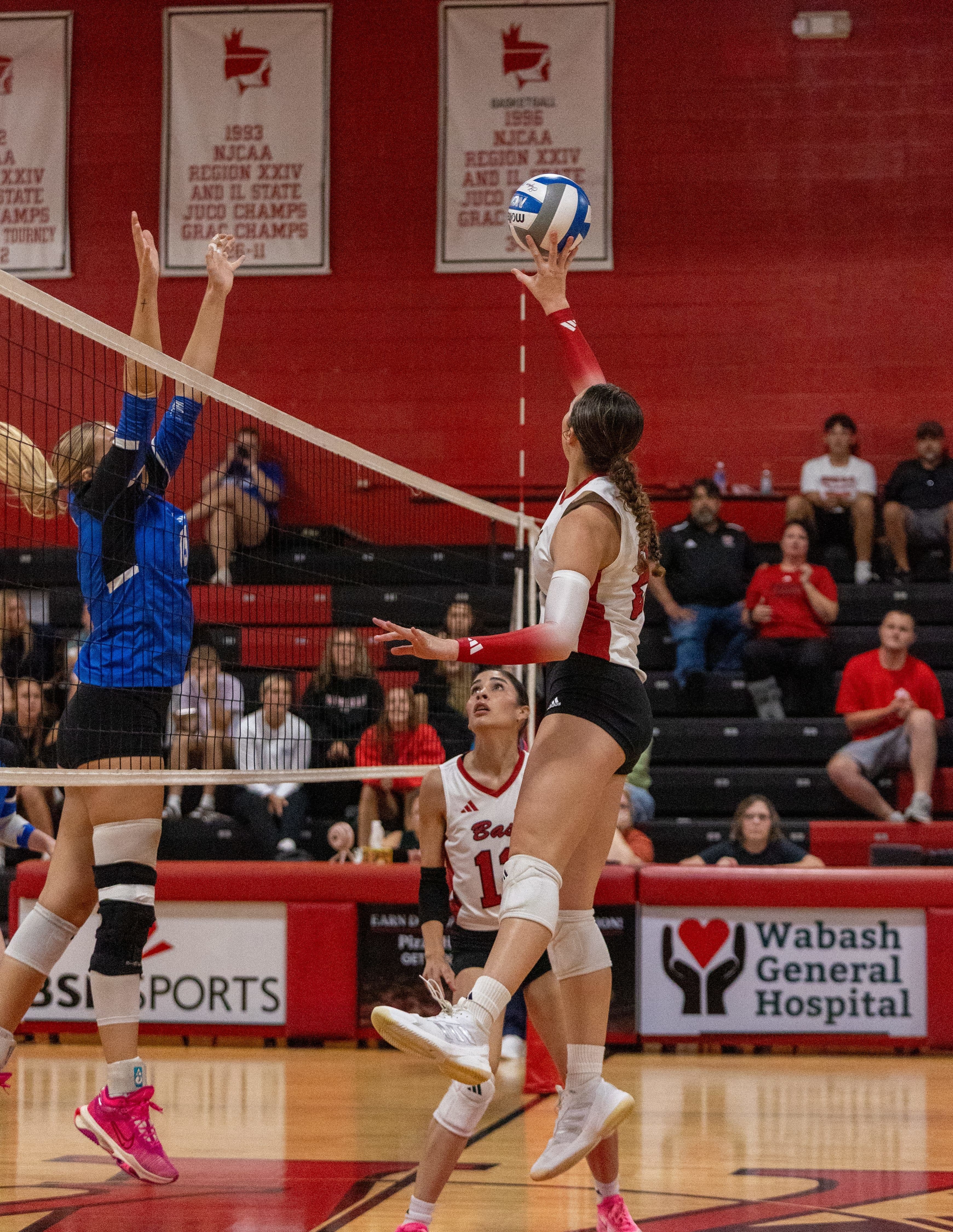 Female college volleyball player jumping to hit the ball over the net.